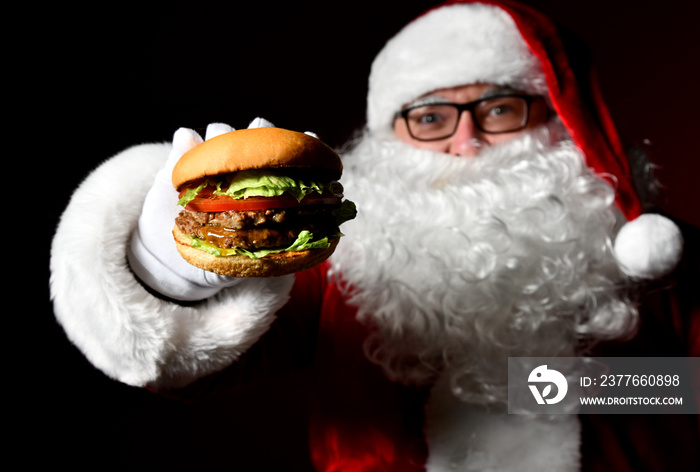 Happy Santa Claus holding offer tasty cheeseburger sandwich hamburger in hand. New year and Merry Christmas