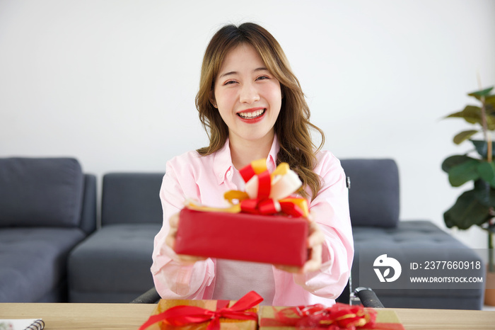 young woman holding and giving gift box to someone on a table in the office