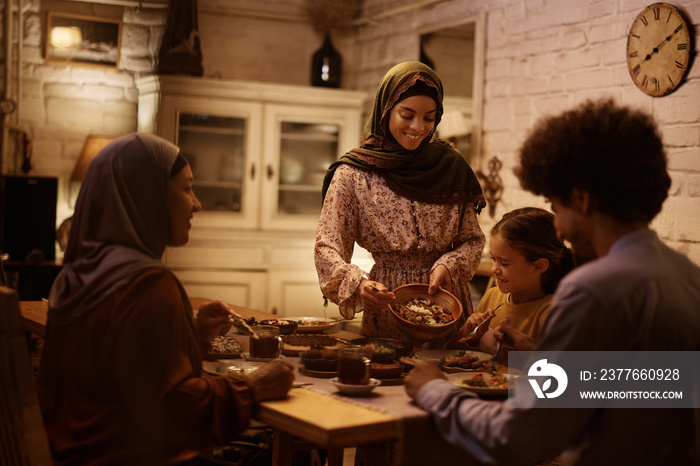 Young Muslim woman serving food to her family at dining table.