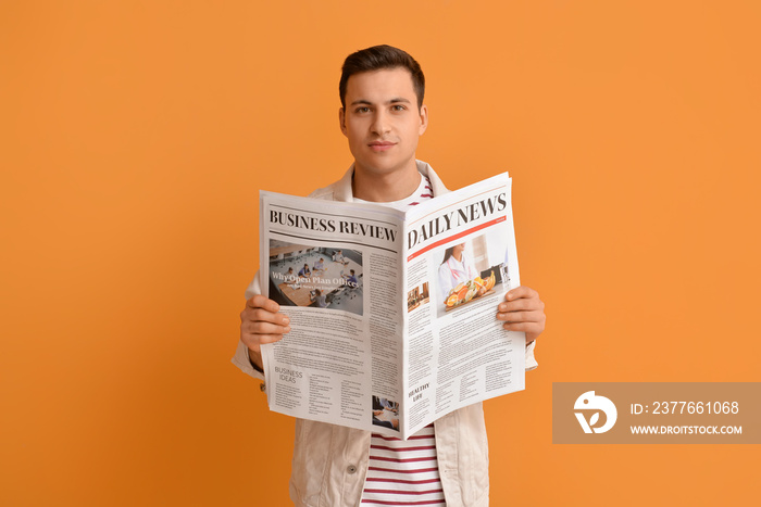 Handsome young man reading newspaper on color background