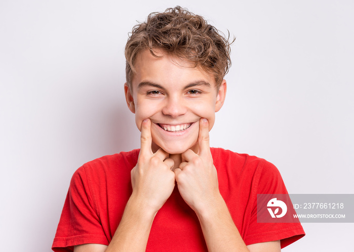 Portrait of teen boy showing his smile. Child pointing with fingers teeth and mouth. Caucasian young teenager on grey background.