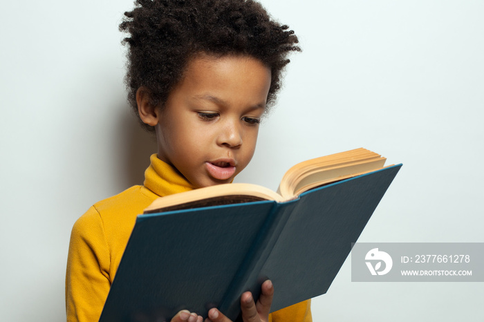 Little African American child boy reading a book on white background. Black kid student portrait