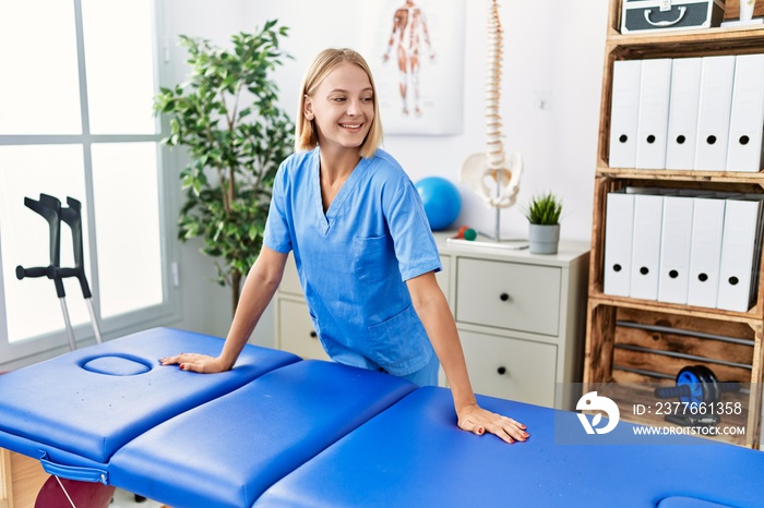 Young blonde woman wearing physiotherapist uniform standing at rehab clinic