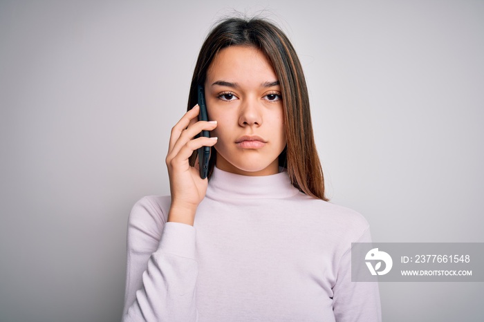 Beautiful brunette girl having conversation talking on the smartphone over white background with a confident expression on smart face thinking serious