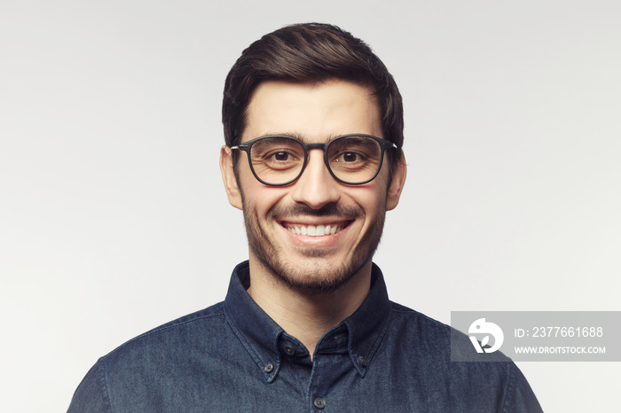 Headshot of smiling handsome male model with trendy haircut and eyeglasses isolated on gray background