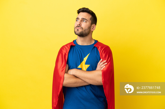 Young handsome caucasian man isolated on yellow background in superhero costume with arms crossed