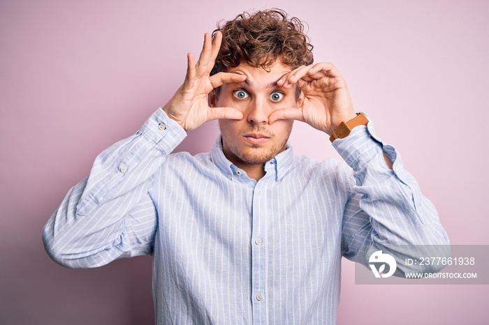 Young blond handsome man with curly hair wearing striped shirt over white background Trying to open eyes with fingers, sleepy and tired for morning fatigue