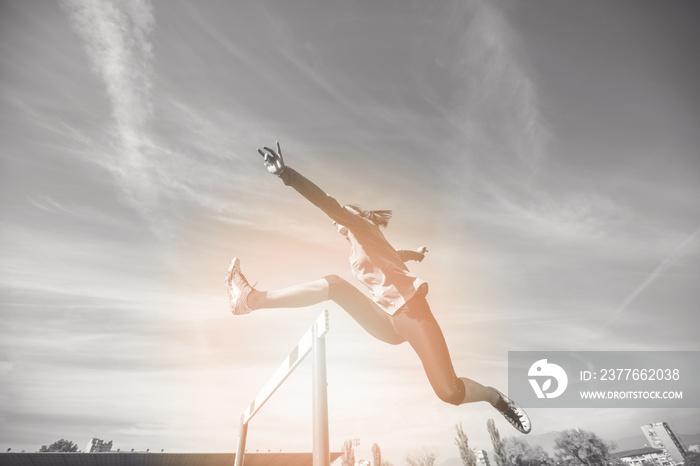 Female athlete jumping above the hurdle during the race