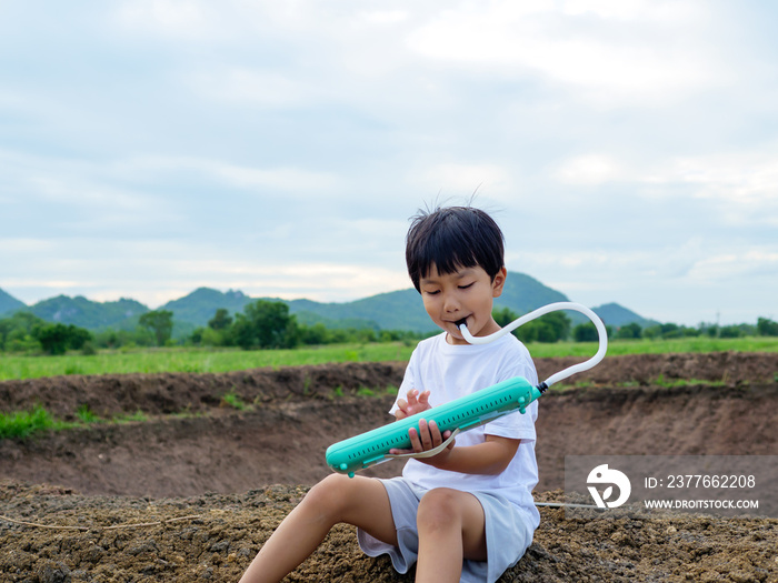 Asian child boy playing, blowing melodeon musical instrument. Kid make music song with happy relaxing face in nature field background. Concept of music, art, young artist, relaxation, freedom peaceful