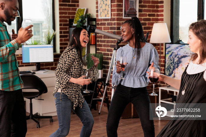 Happy, cheerful, laughing asian girl dancing accompanied by smiling, glad african american lady. Various ethnicities people, partners drinking wine, hanging around at friends reunion.