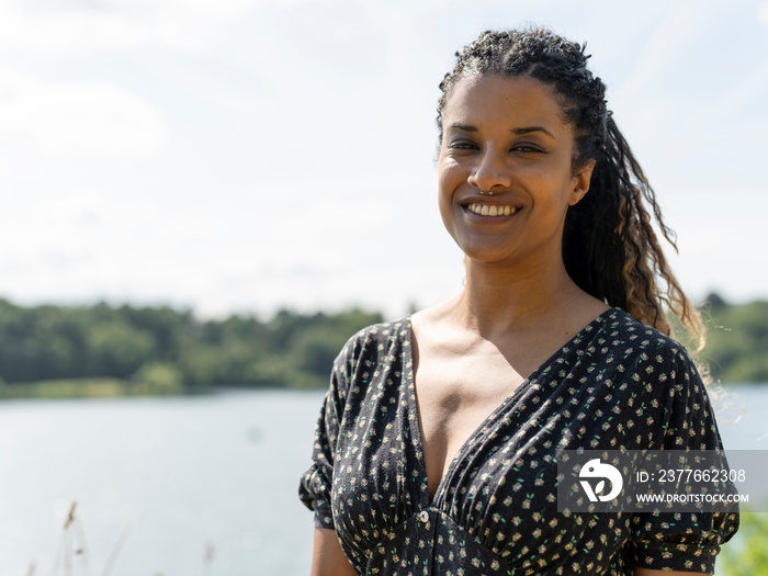 Portrait of smiling woman standing by lake sunny day