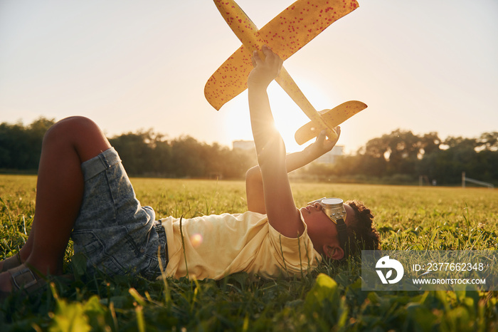 In glasses with toy plane. African american kid have fun in the field at summer daytime