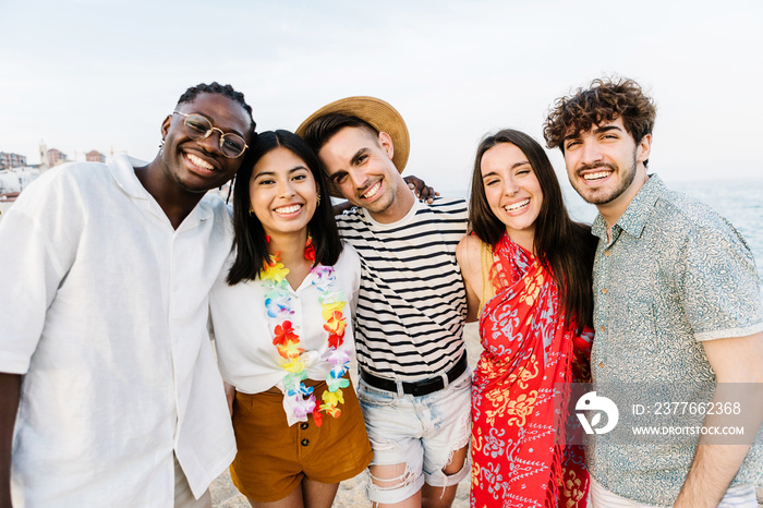 Group portrait of multiracial young friends outdoors in summer - United five millennial people hugging each other smiling at camera at party beach