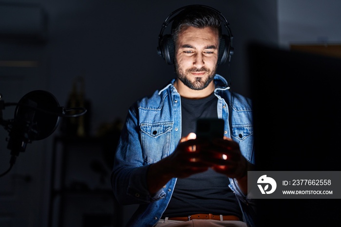 Young hispanic man artist smiling confident using smartphone at music studio