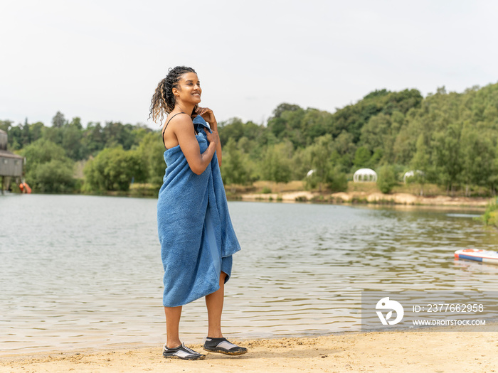 Smiling woman standing wrapped in towel by lake