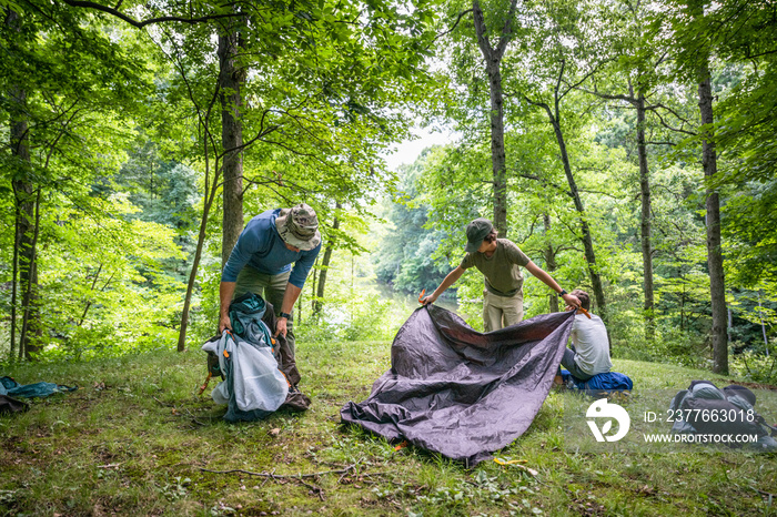 Air Force service member sets up a tent with his sons on  a backpacking trip.