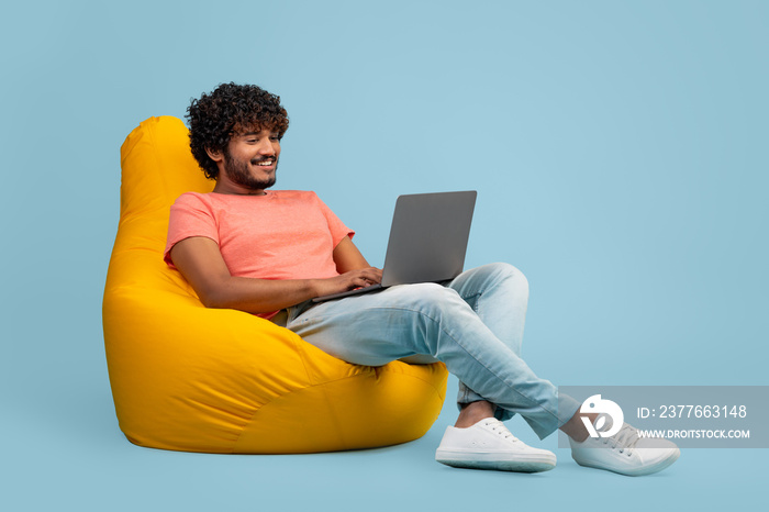 Handsome indian guy using modern notebook on blue