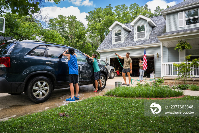 Air Force service member washes his vehicles with his sons in the driveway.