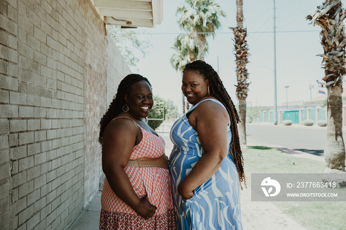 2 plus size women stand and look over their shoulders