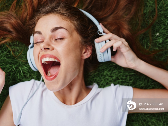 Woman open mouth surprise lying on green grass with headphones spread her hair on the ground in summer