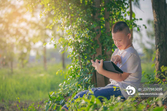 Asian Dawn syndrome boy enjoying outdoors using touch pad for self learning at outdoor backyards. Technology for education concept.