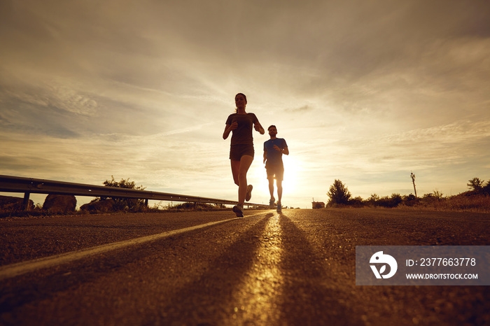 A guy and a girl jog along the road at sunset in nature. The couple is running.