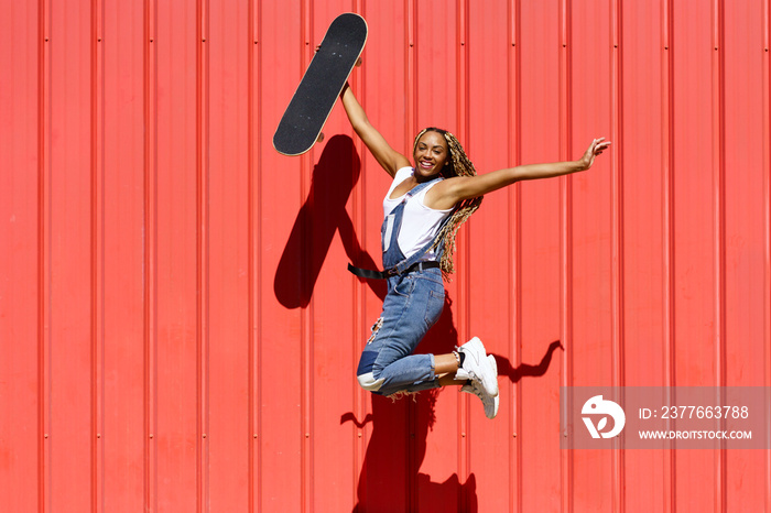 Carefree black woman with skateboard jumping in city