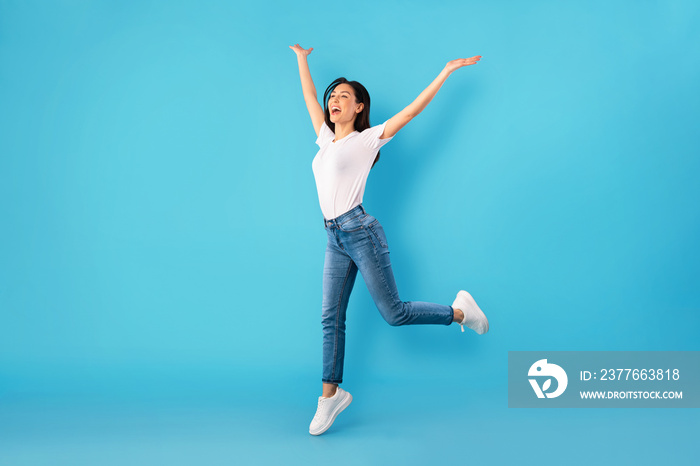 Happy woman jumping over blue studio wall