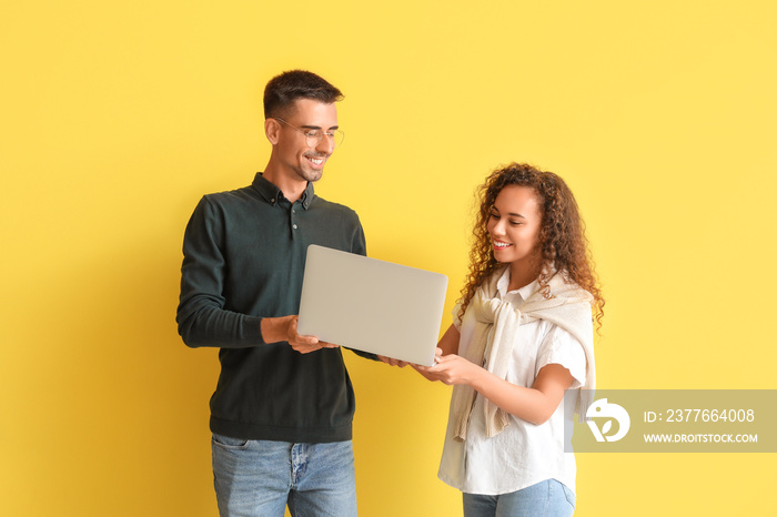 Young couple using laptop on yellow background