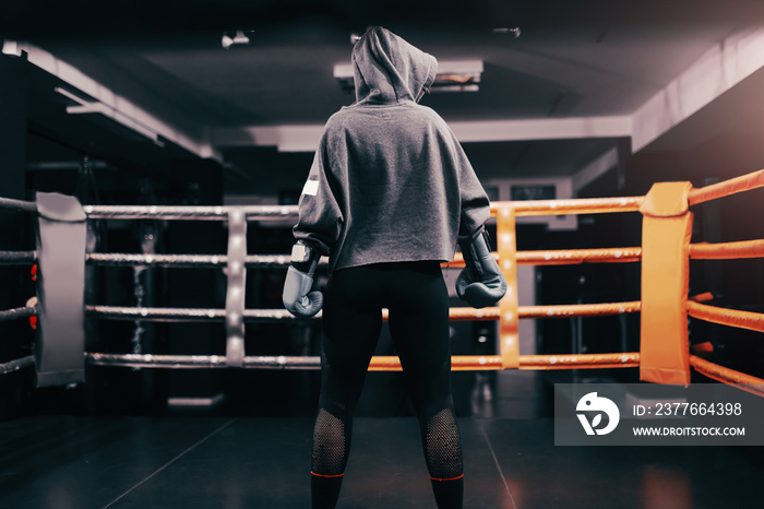 Boxer girl with hoodie and boxing gloves on standing in ring with backs turned.