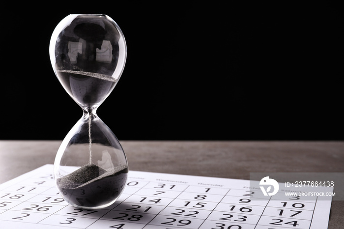 Crystal hourglass with calendar on table. Deadline concept