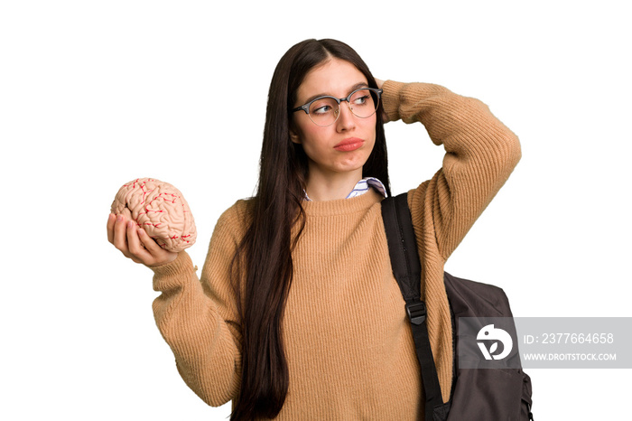 Young caucasian student woman holding a brain isolated touching back of head, thinking and making a choice.