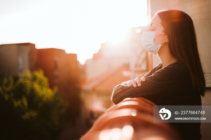 young woman at home on a terrace wearing protective mask and enjoying a sunny day. Corona virus Covid-19 concept