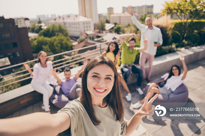 Photo of smiling cheerful positive good mood group of best friends take selfie showing v-sign on rooftop outside