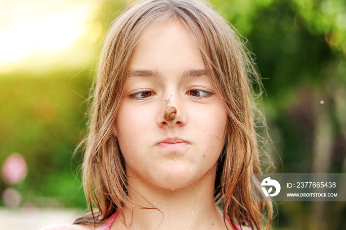 Funny preteen girl looking at snail on her nose. Selective focus on eyes, face close up. Curious childhood. Summer holidays leisure time