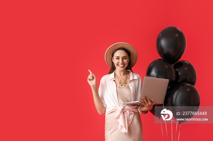 Happy young woman with laptop and balloons showing something on color background. Black Friday sale