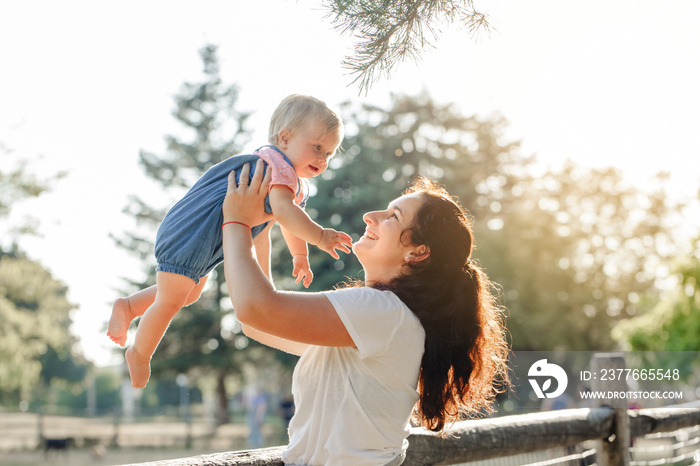 Mothers Day holiday. Young smiling Caucasian mother and girl toddler daughter hugging in park. Mom holding child baby on summer day outdoor. Happy authentic family childhood lifestyle.