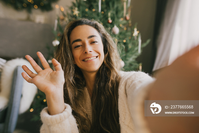 Young woman waving her hand, video chatting with family and friends on Christmas.