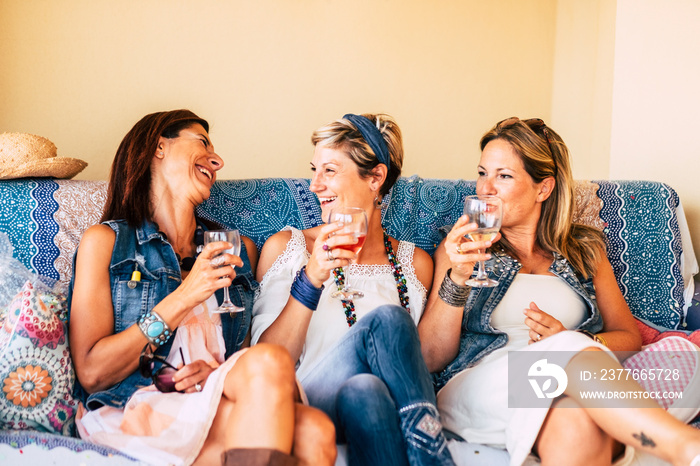 Three friends women laugh and have fun sit down on a sofa - people in friendship at home - trendy young ladies - caucasian trendy adult females drinking red wines together