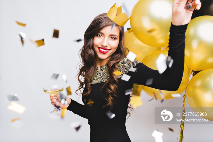 Crazy party time of beautiful women in elegant black dress and yellow crown celebrating new year, birthday, having fun, dancing, drinking alcohol cocktails.Emotion face, red lips, gold balloons