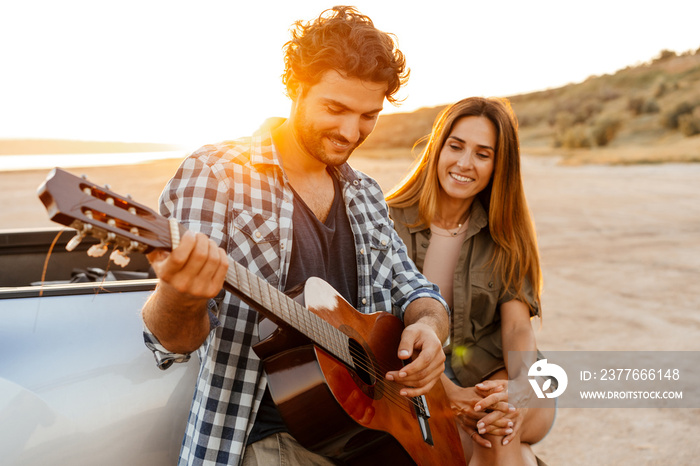 White man playing guitar during travel on car with his girlfriend