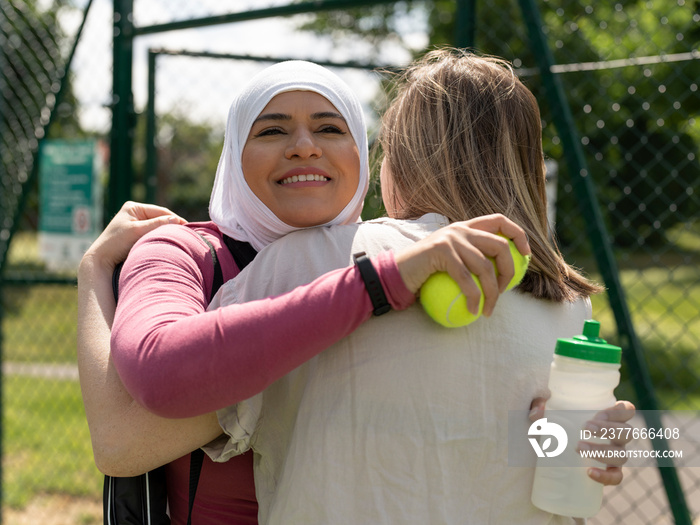 UK,Sutton,Smiling woman in headscarf embracing friend at tennis court