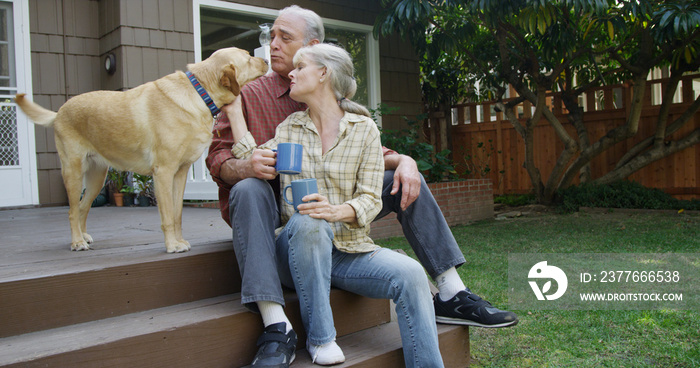 Senior couple having coffee petting dog in their yard