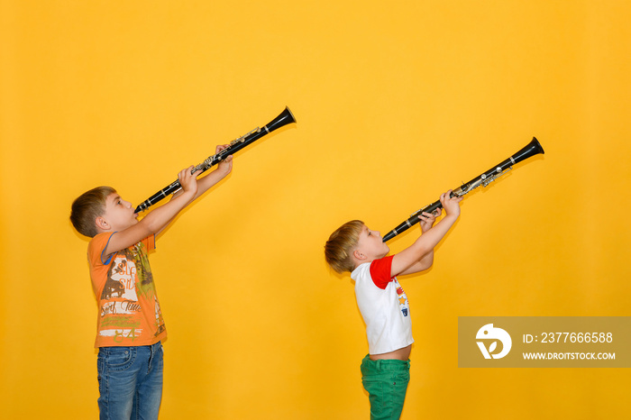 Two boys play the clarinet and hold it up, on a yellow background.