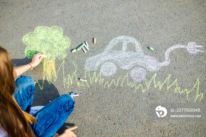 Little girl with creative craft hobby drawing electro on the asphalt with chalk car environment, eco friendly, save energy in park at summer day