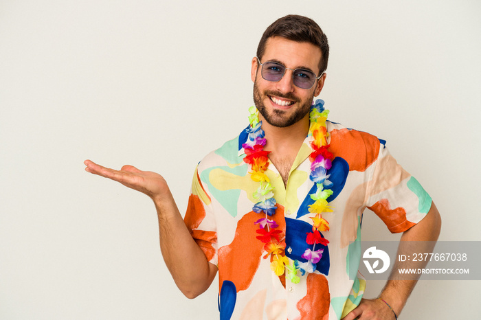 Young caucasian man dancing on a hawaiian party isolated on white background showing a copy space on a palm and holding another hand on waist.