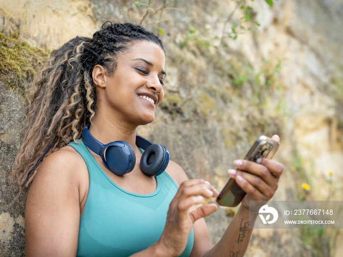 Smiling woman using smart phone against rock