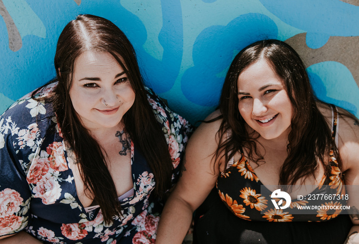 2 sisters sit against a blue wall