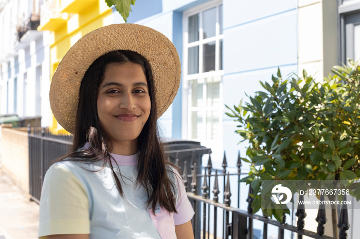 Portrait of smiling young woman in sun hat standing in street