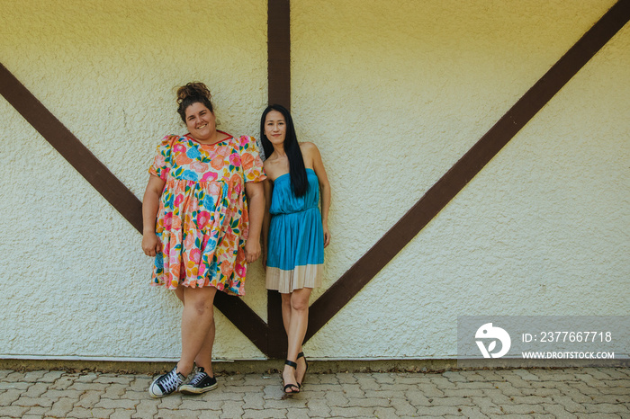 2 friends wearing dresses stand against a wall